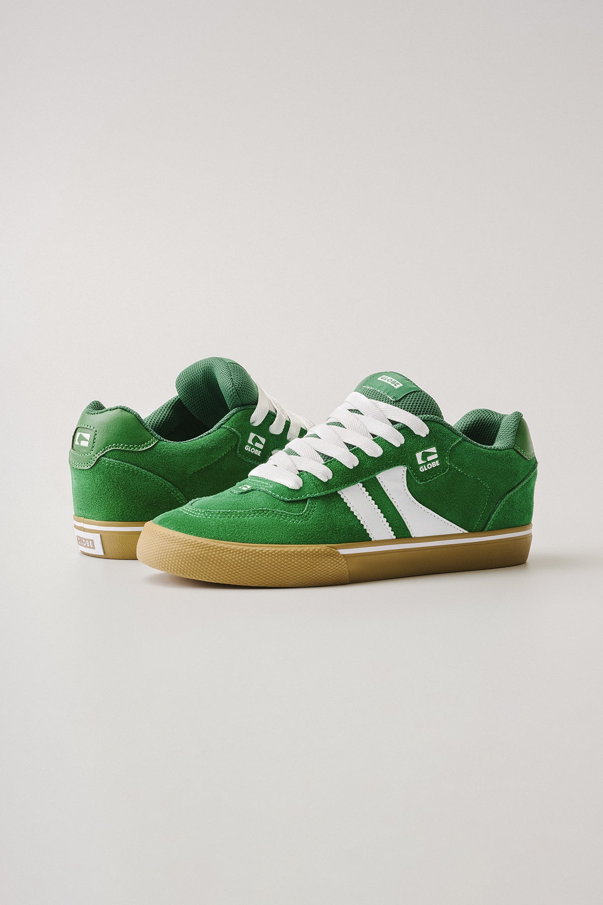 The Encore-2 sneakers in Green/White/Gum feature suede uppers, white laces and side stripes, and a gum sole. Displayed on a plain light background, one shoe stands upright while the other is angled to show its inner side.