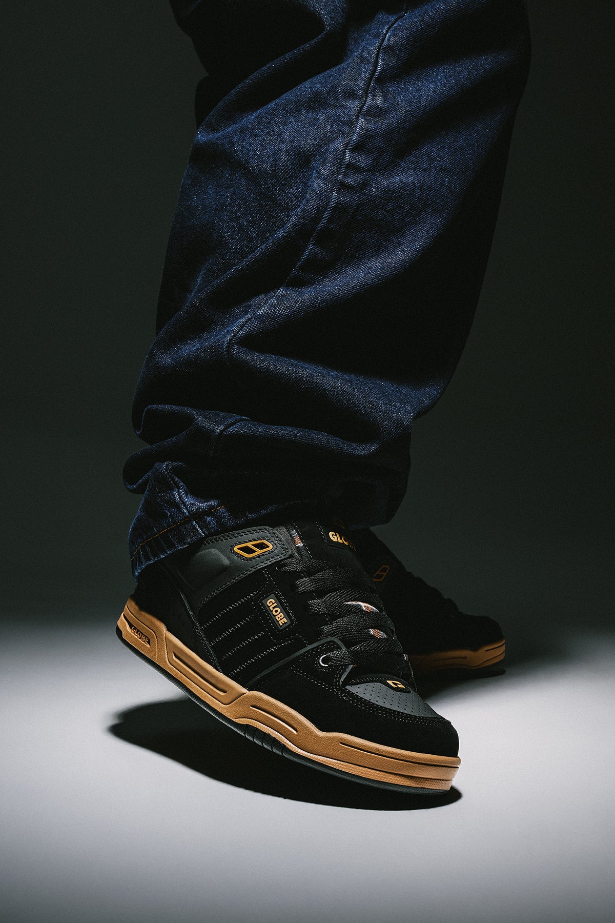 Foot in Fusion sneakers shows black upper with tan sole and dark denim jeans