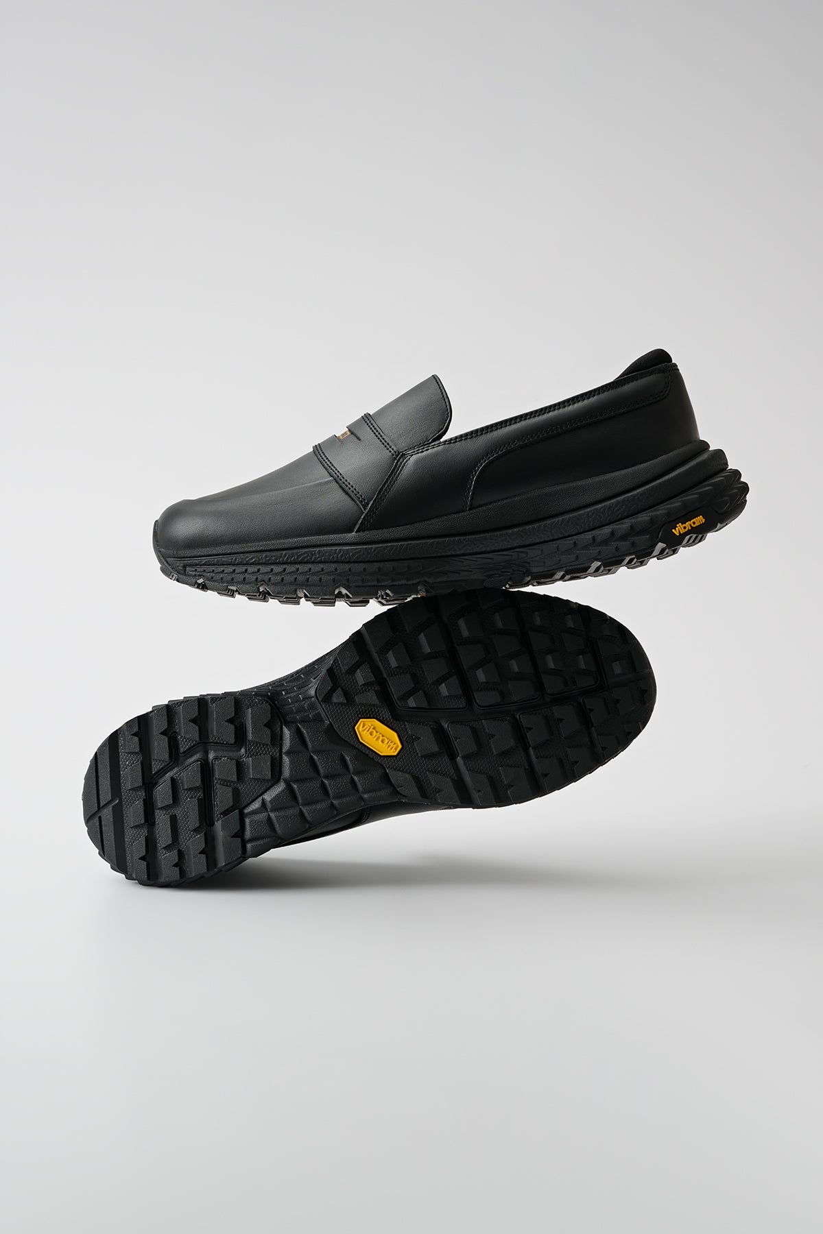 The Liaizon Vibram - Black features a classic lace-up design in black leather, shown with one shoe upright and the other on its side to display the textured rubber sole against a plain gray background.