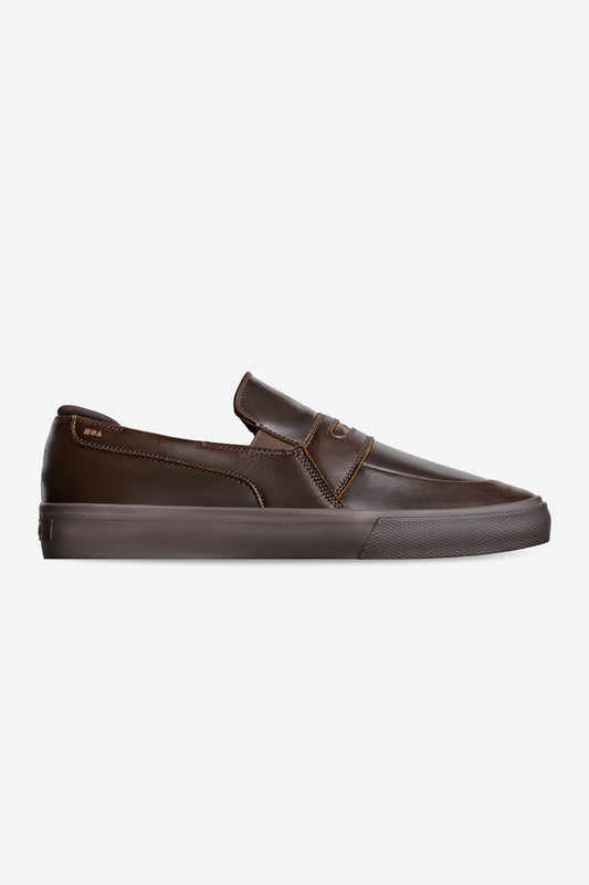 The Liaizon - Dark Brown is a low-profile, slip-on sneaker with a round toe and rubber sole, crafted from dark brown leather and displayed in side view against a plain white background.