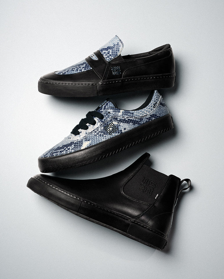 Three Melbek - Wasted Talent Black/Snake skate shoes are arranged diagonally on a gray background: a black suede slip-on, a blue and white tie-dye lace-up, and another black slip-on with pull tab, all with thick black soles and subtle side branding.