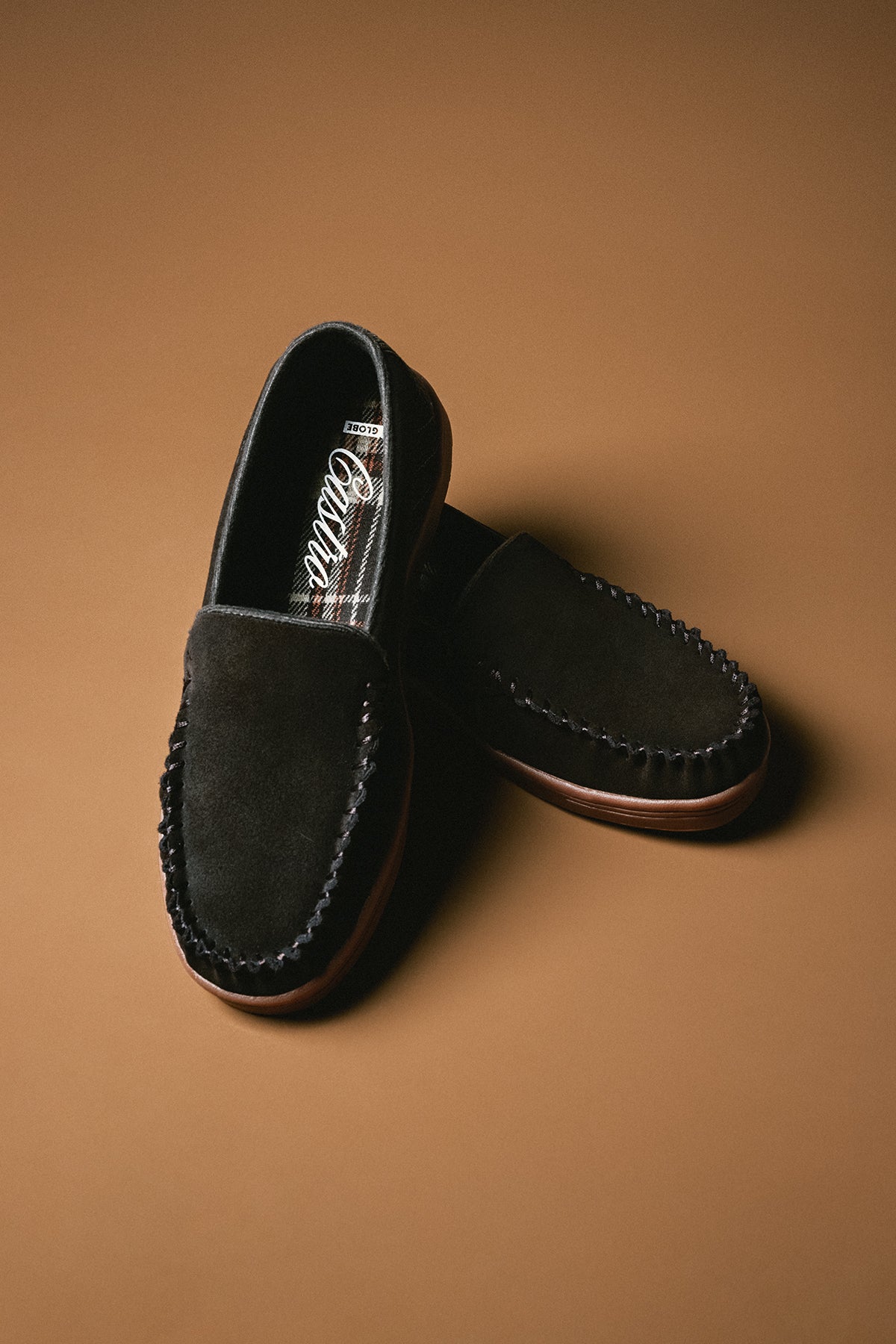 Castro dark suede moccasin toe loafer with tartan lining and brown sole on a warm tan backdrop