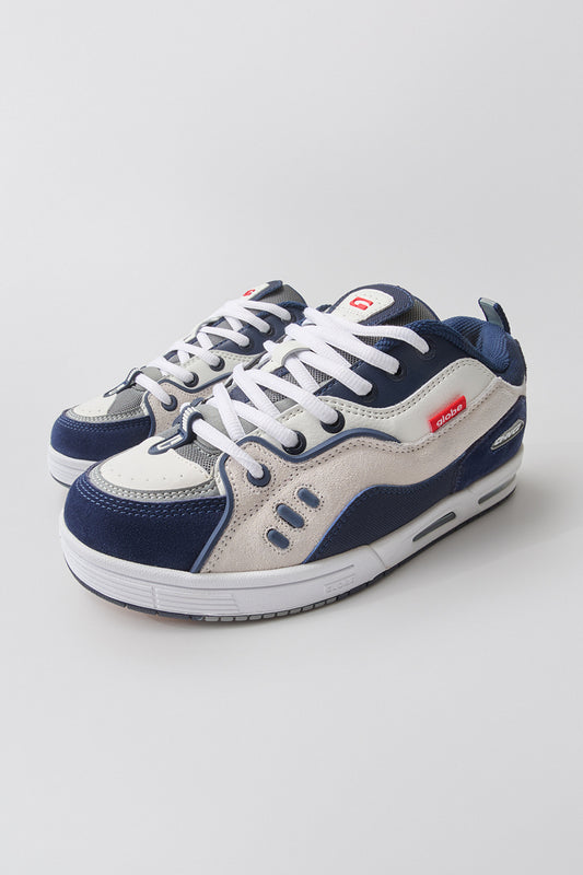 A pair of CT-4 - White/Navy Globe skate shoes, featuring navy blue, white, and gray panels with white laces and a small red brand tag on the side, displayed against a plain light background.