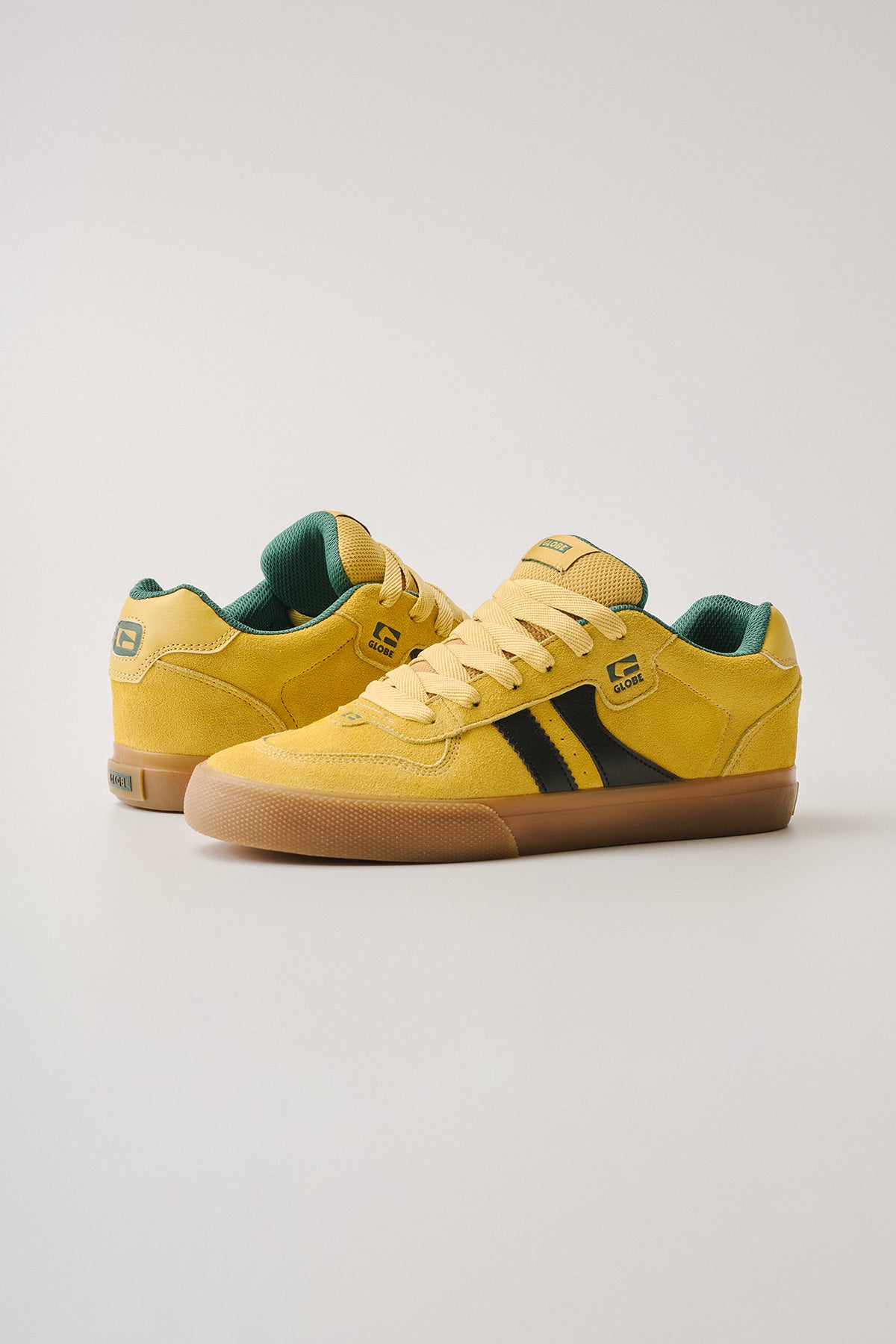 The Encore-2 - Yellow/Green sneakers feature yellow low-top uppers with black side stripes, green inner lining, gum soles, and Globe logos on the tongue and heel, presented against a neutral background.