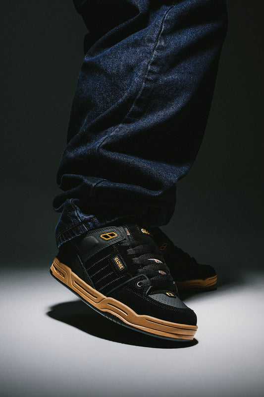 Foot in Fusion sneakers shows black upper with tan sole and dark denim jeans