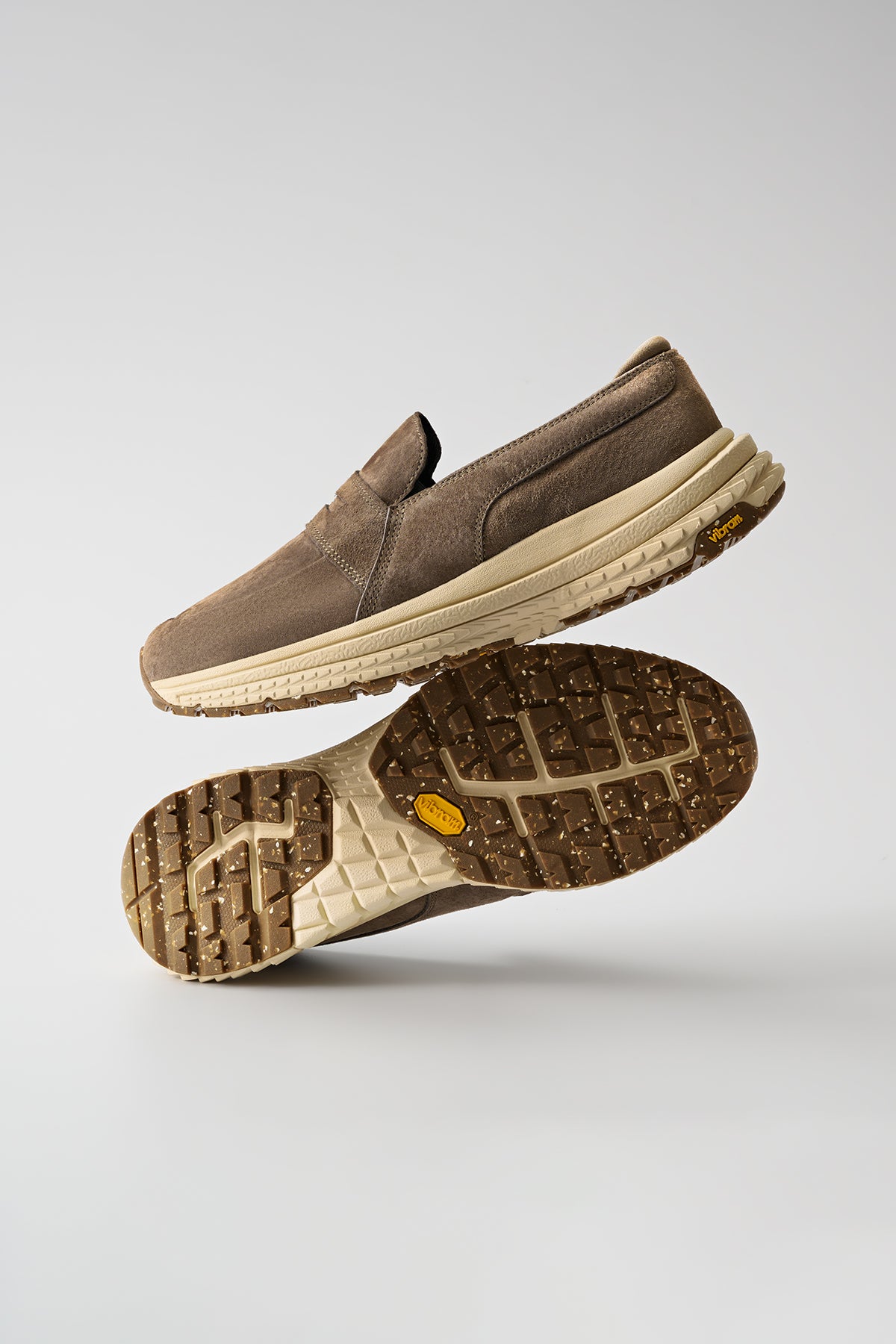 The Liaizon Vibram - Walnut slip-on sneakers with beige soles are displayed on a plain background, one atop the other, showing the textured rubber tread and minimalist design.