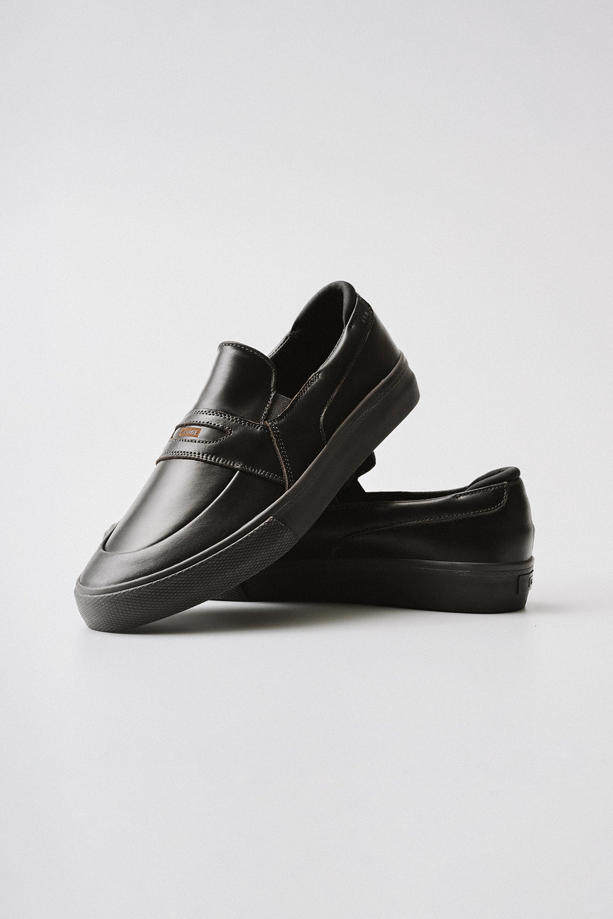 A pair of dark brown Liaizon slip-on loafers with stitching details, one upright and the other lying flat beneath it, displayed on a plain light background.