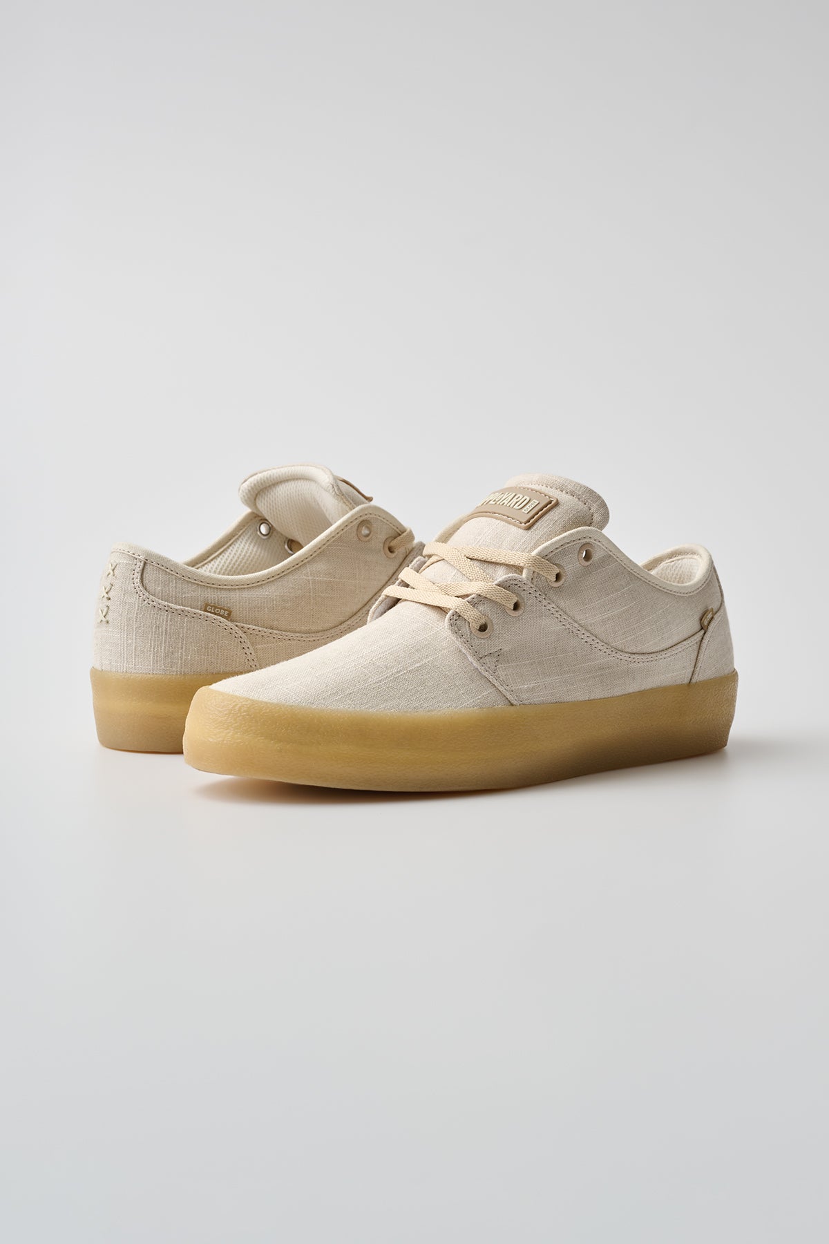 The Mahalo - Hemp/Crepe sneakers in beige canvas with light brown rubber soles are showcased on a plain light gray background; one shoe faces forward while the other is angled to display the side and heel.