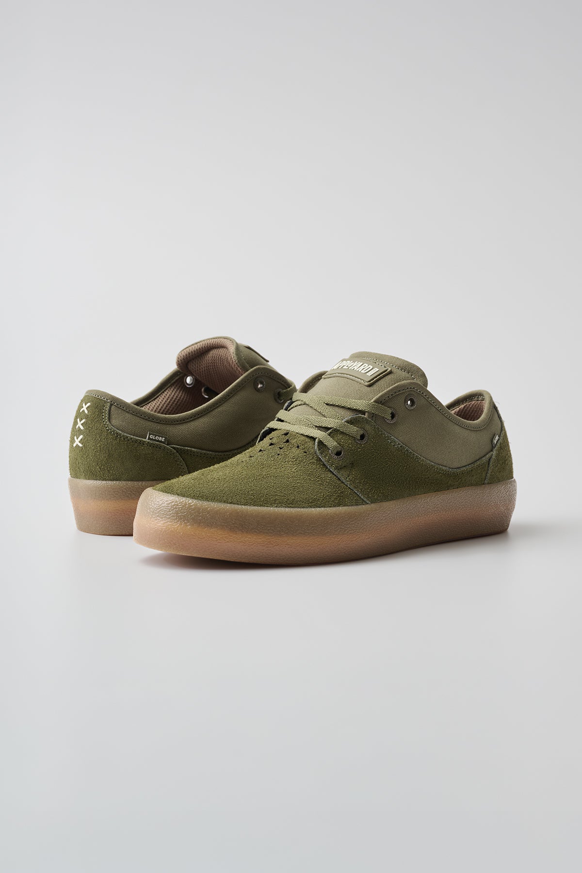 The Mahalo - Military Olive/Crepe are olive green suede low-top sneakers with gum rubber soles, laces, and white stitched accents on the back heel, shown against a plain light background.