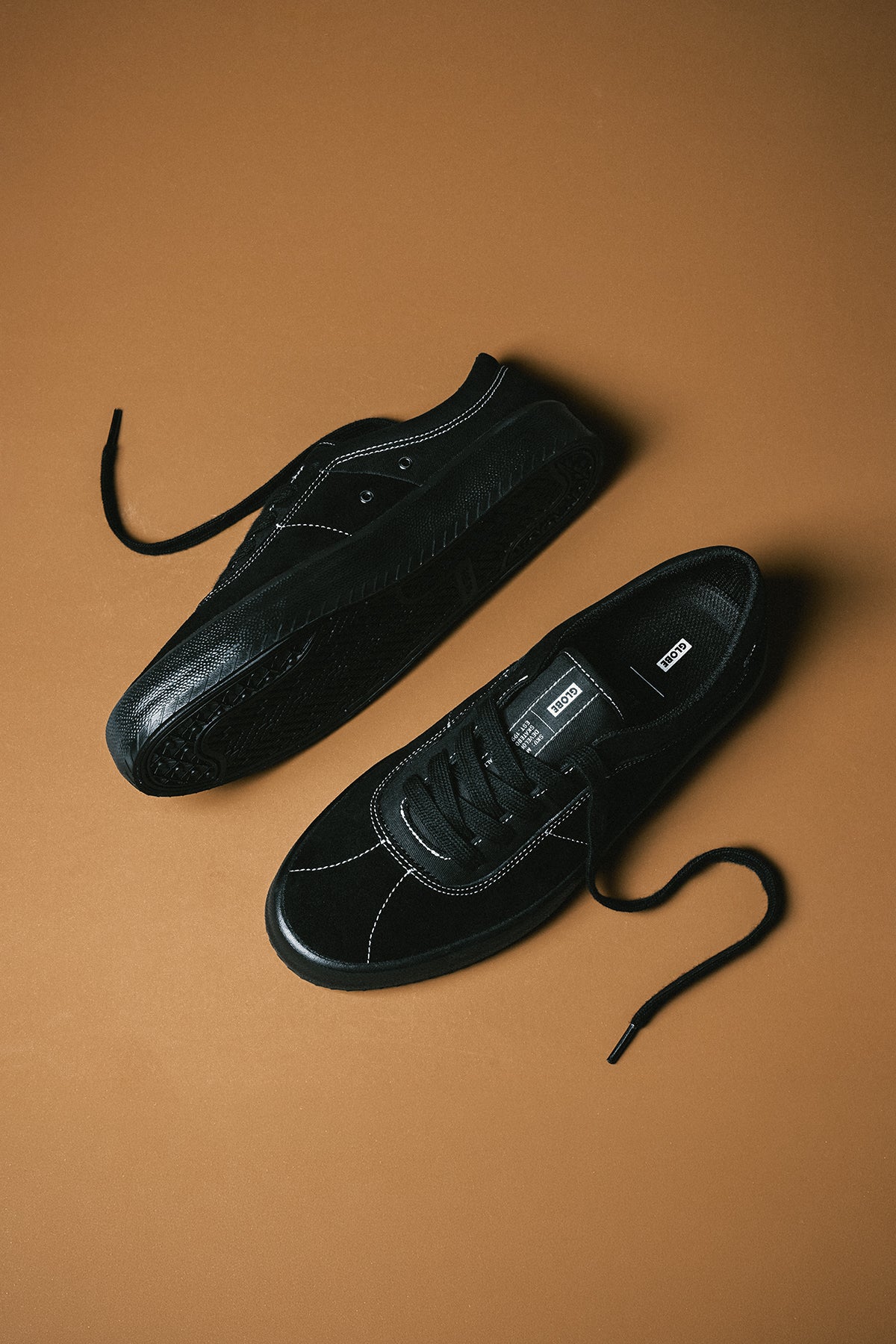 Flat lay of black Melbek sneakers with untied laces on a brown background