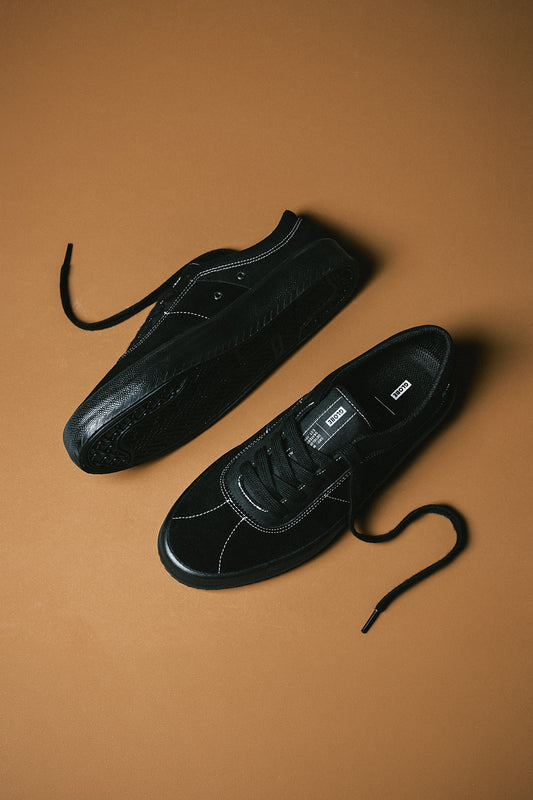 Flat lay of black Melbek sneakers with untied laces on a brown background