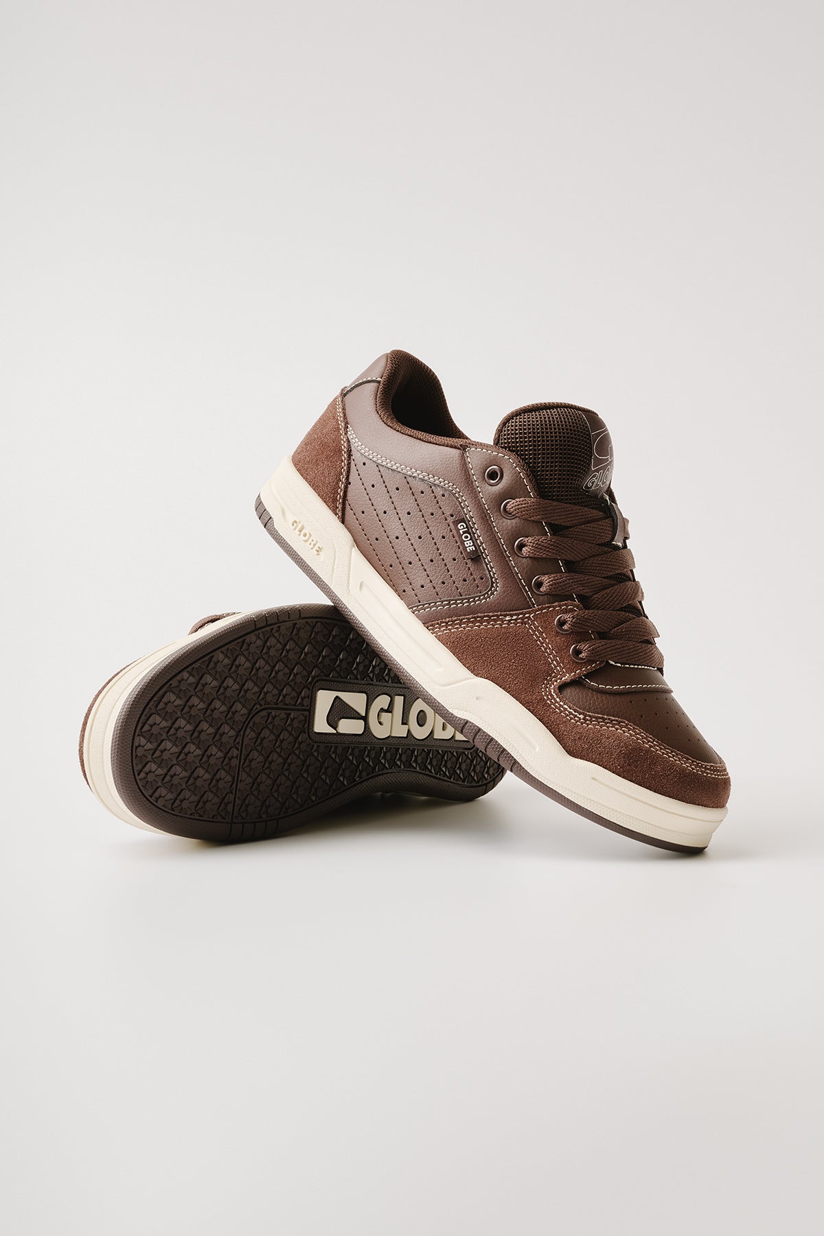A pair of Mojo 2.0 - Brown/Antique skate shoes; one stands upright while the other is tilted to reveal the cream-colored sole with textured grip and Globe logo underneath.