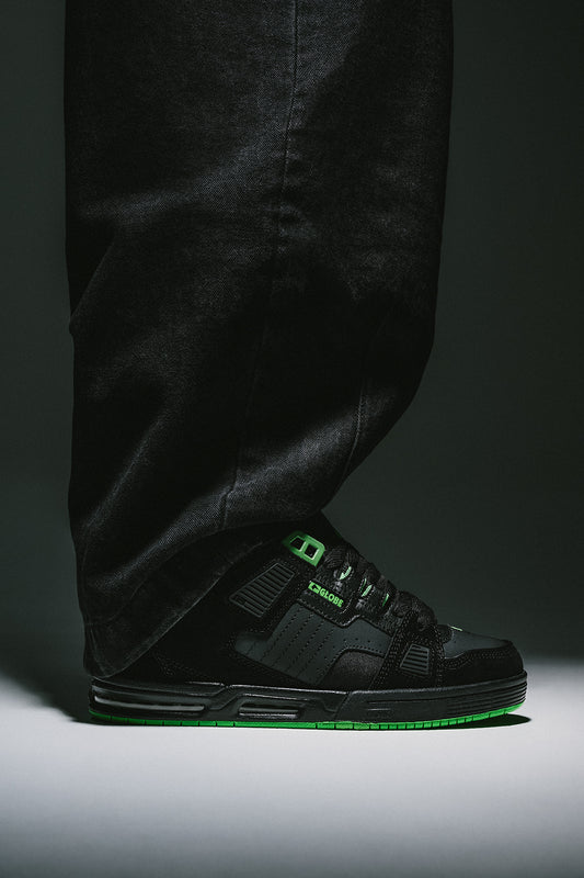 Globe Sabre black skate shoe with green accents and neon green sole worn with dark pants
