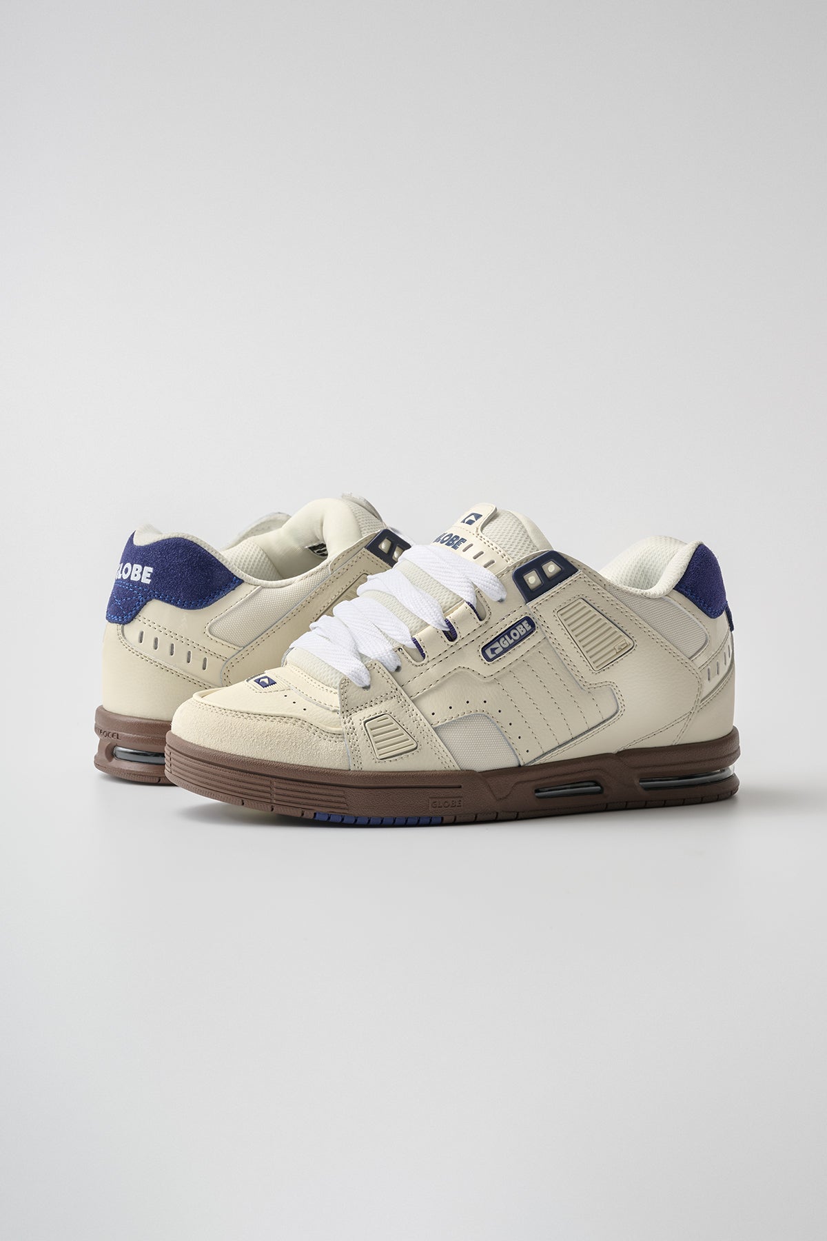 The Sabre - Antique White/Blue features cream skate shoes with brown soles, navy blue accents, and white laces, set against a plain light gray background.