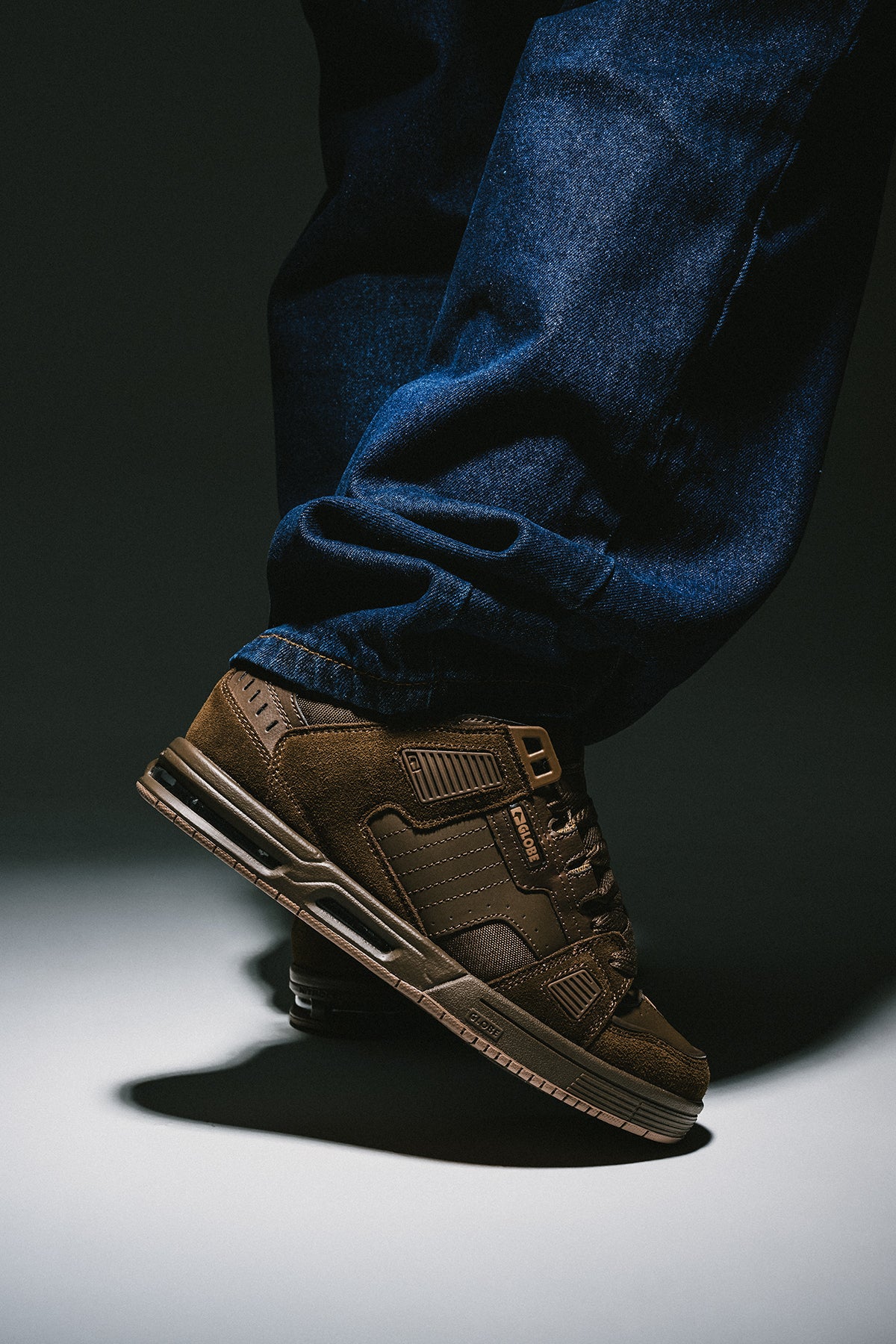Side view of a brown Globe Sabre skate shoe on a denim leg, showing the padded collar and rugged build