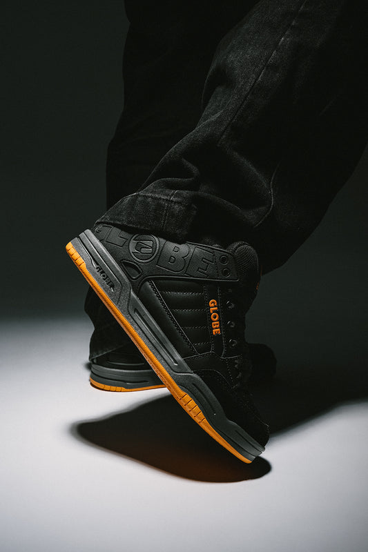 Tilt skate shoe in black with orange outsole shown from the heel side with embossed Globe branding.