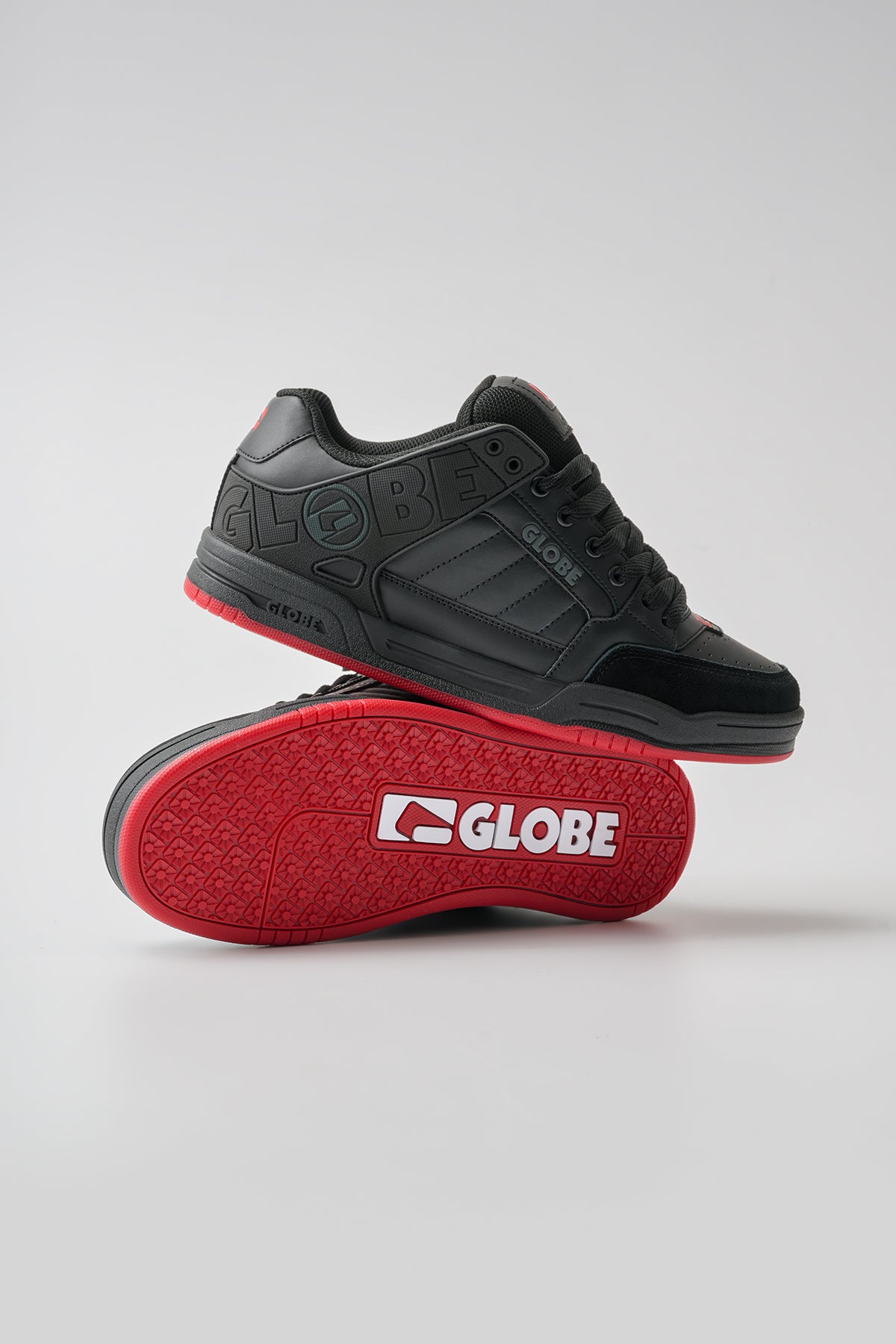 The Globe Tilt in Black/Red/Charcoal features embossed branding, red accents, and red soles with a white Globe logo. One shoe is upright; the other lies on its side to display the vibrant red sole.
