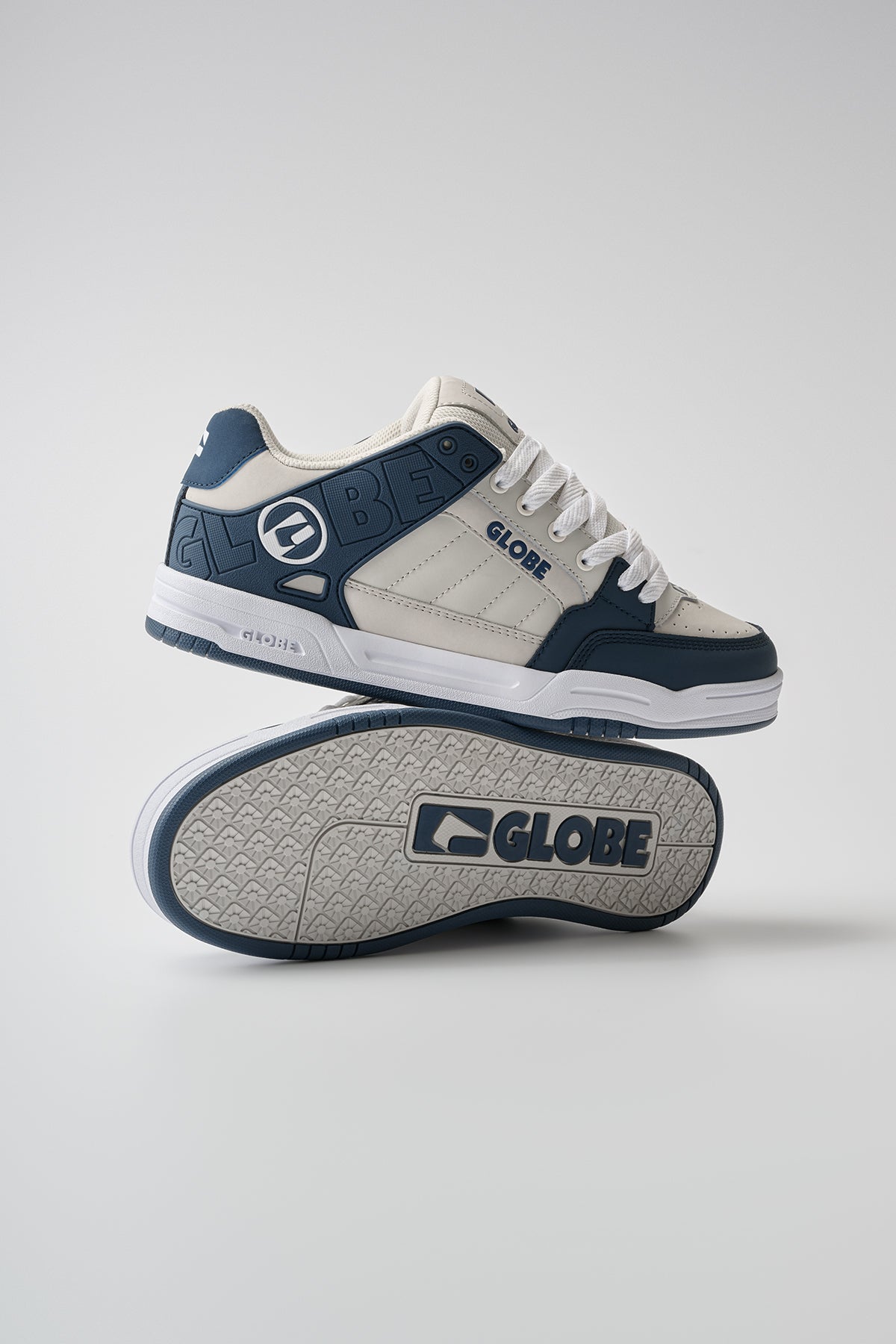 A pair of Globe Tilt skate shoes in blue and grey—one upright, one showing the sole. The Globe logo is visible on both the side and the sole.