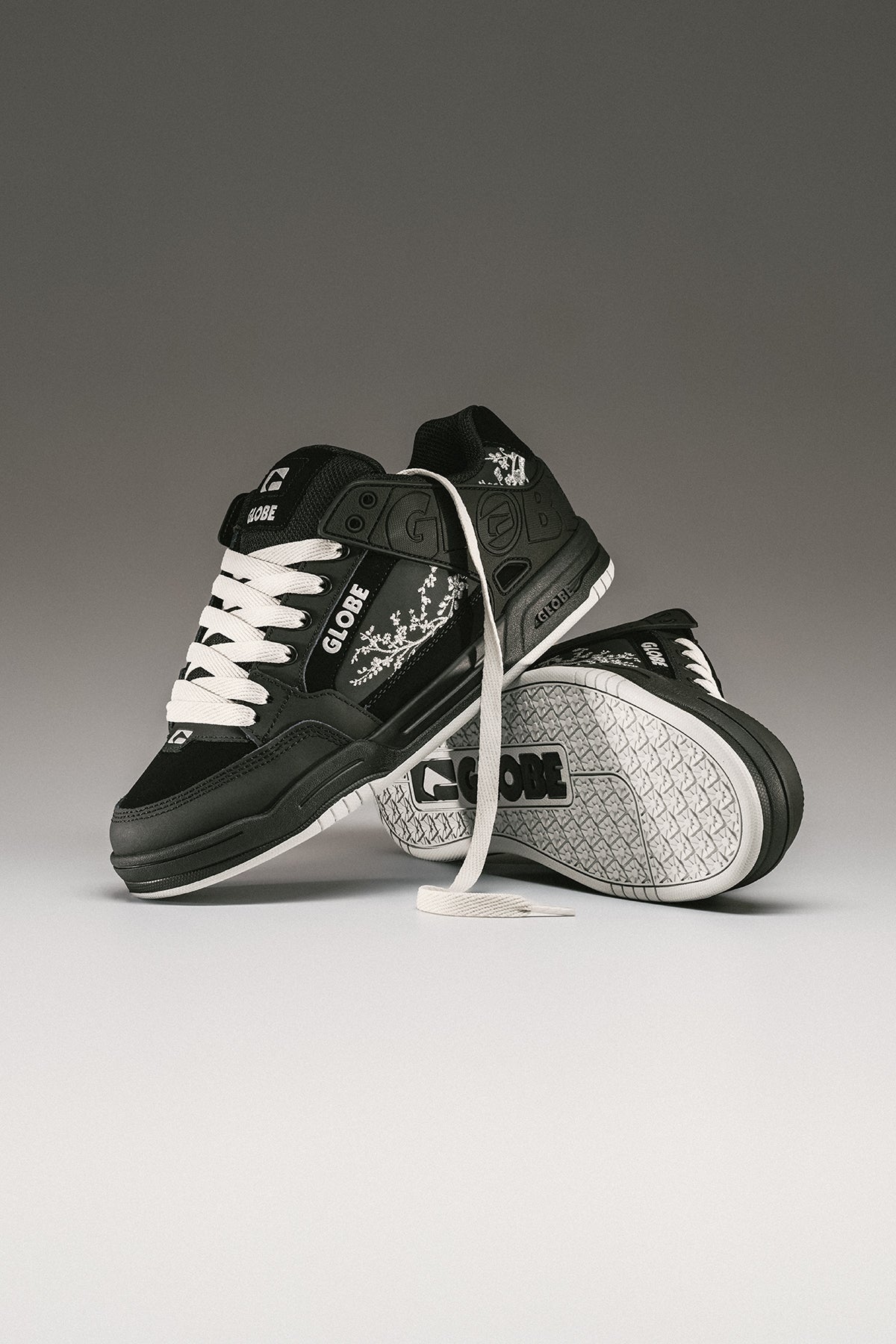 Studio shot of Tilt black Cherry Blossom sneakers with white laces and floral embroidery
