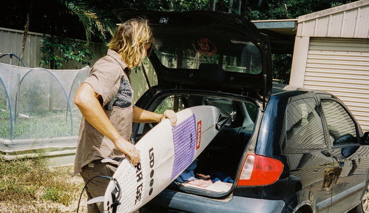 Noa Deane loading surfboard into car 