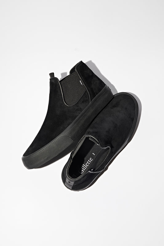 The Dover - Black Suede/Gillette features black slip-on suede skate shoes with rubber soles, shown one upright and one on its side against a white background, highlighting their comfort and durability.