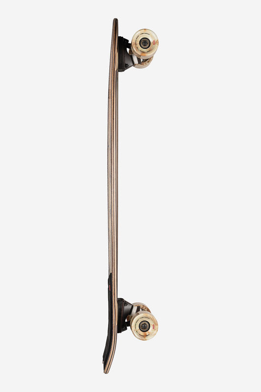 A side view of the Chromantic Cruiserboard 33" - White Oak/Jaguar, highlighting its surf-inspired wooden deck, upward-curved tail, and four beige wheels on black trucks, isolated on a white background.