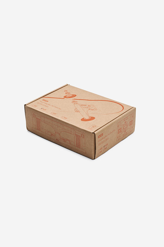 A closed brown cardboard box with red line drawings and product details, including "Everything But The Deck Kit Accessories Hg 5.0\" - Raw Finish," sits on a plain white background—ideal for skateboard kits or components.